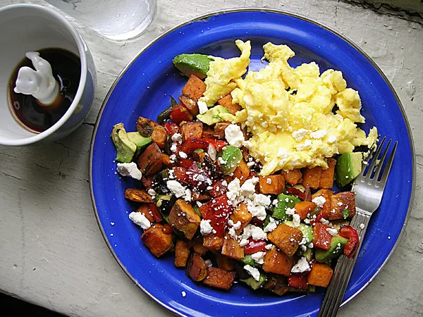 A vibrant assortment of AIP-friendly breakfast dishes including coconut yogurt with fresh berries, sweet potato hash, bone broth soup, and wild salmon with greens, arranged beautifully on a rustic wooden table.