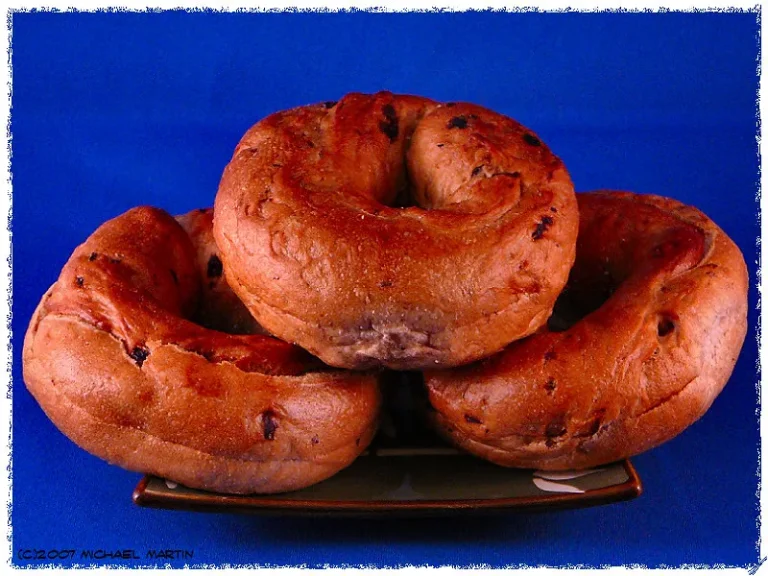 Golden cinnamon raisin bagels with a shiny crust stacked on a rustic wooden board, showcasing their chewy texture and studded raisins.
