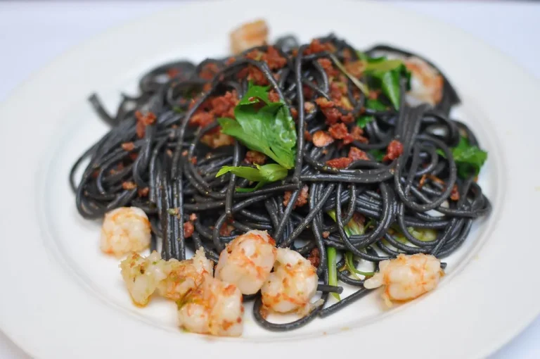 Elegant black spaghetti with squid ink sauce and shrimp, garnished with parsley and served on a white ceramic plate.