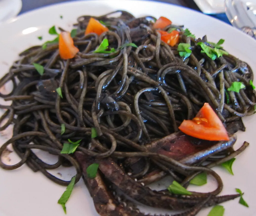Black spaghetti with squid ink sauce topped with shrimp and parsley on a white plate