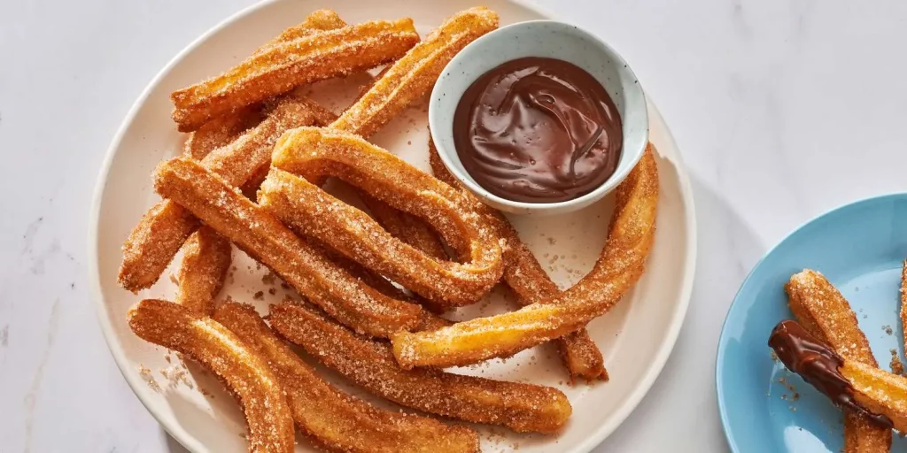 Churros coated in cinnamon sugar served with a rich chocolate dipping sauce in a rustic tray.