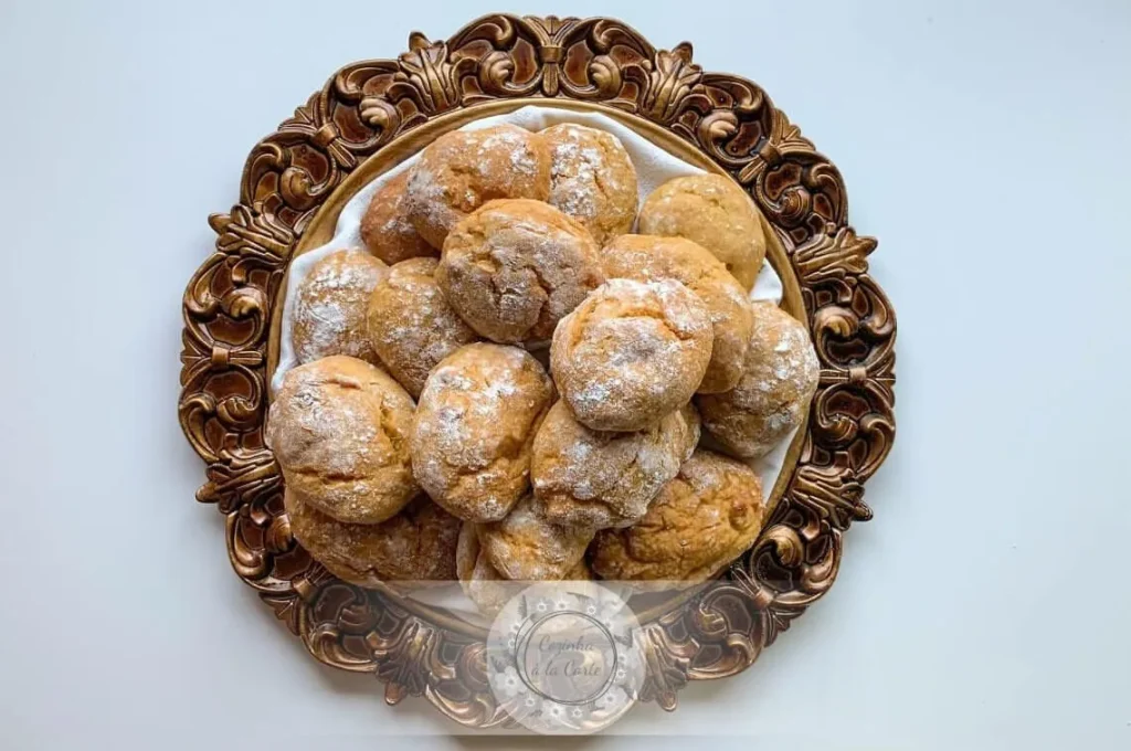 Golden Pão de Deus buns topped with a sweet coconut mixture, served on a rustic plate for a traditional Portuguese breakfast.