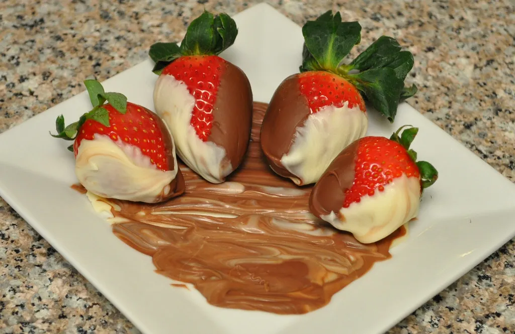 Strawberries and orange slices dipped in dark chocolate and arranged on parchment paper