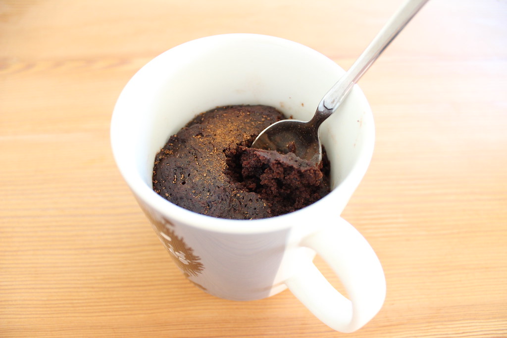Rich and gooey chocolate mug cake in a white ceramic mug, topped with melted chocolate chips and a dusting of cocoa powder.