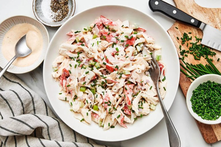 Delicious and creamy imitation crab meat salad served in a white bowl garnished with fresh herbs