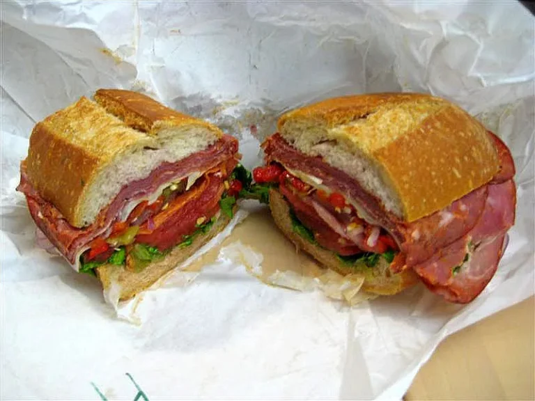 Layered Italian deli sandwich with cured meats, provolone cheese, lettuce, tomato, and onions on a toasted hoagie roll