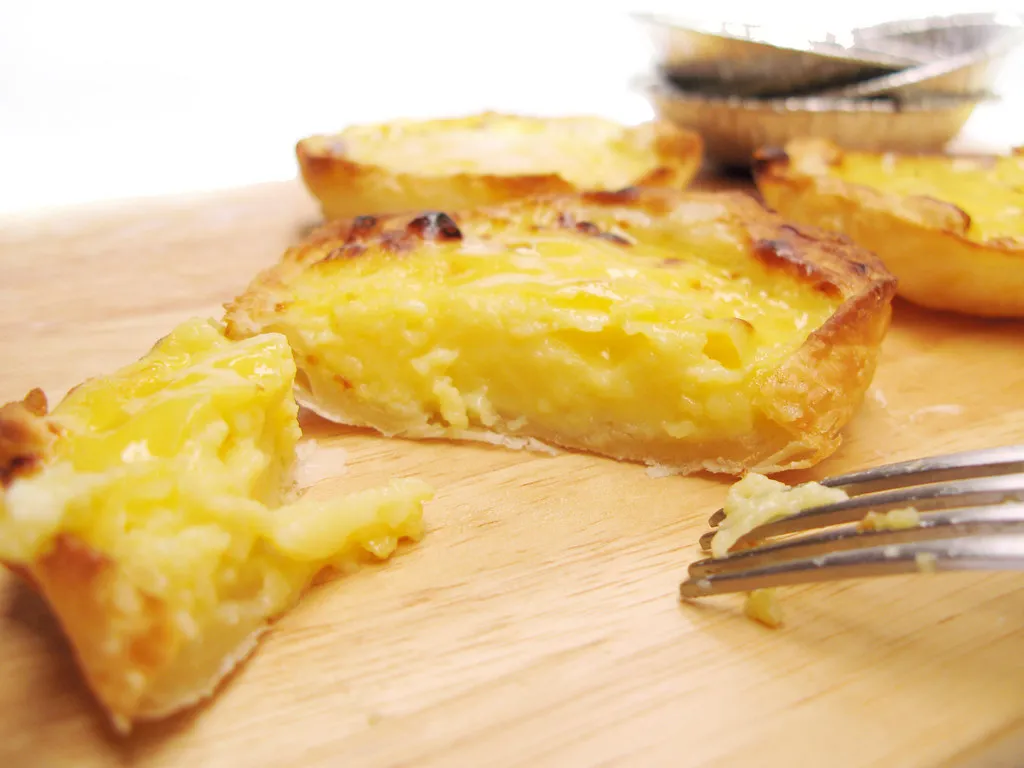 Close-up of freshly baked Pastéis de Nata with caramelized custard tops and flaky puff pastry crust, dusted with cinnamon.