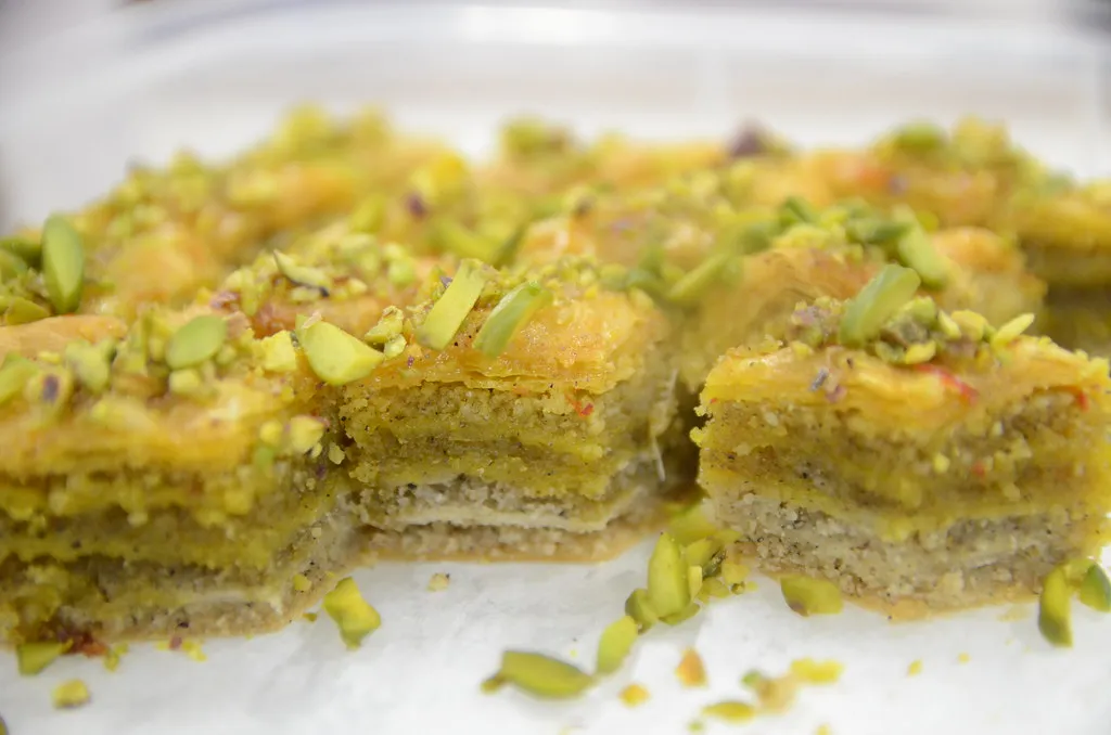 Close-up of golden, flaky baklava layers filled with chopped nuts and drizzled with honey syrup, garnished with crushed pistachios.