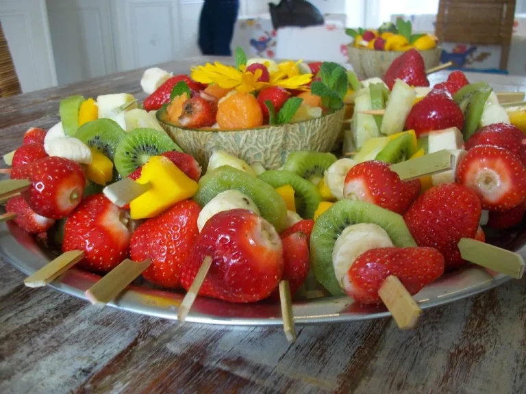 A vibrant summer dessert platter with fresh fruit skewers, mini cheesecake cups, chocolate-dipped strawberries, and watermelon feta mint bites on a wooden board”