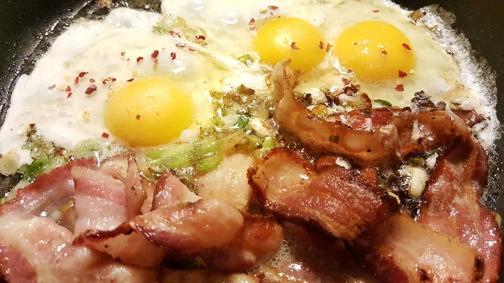 Hearty breakfast skillet with crispy hash browns, scrambled eggs, crumbled bacon, and melted cheddar cheese served in a black cast iron pan.