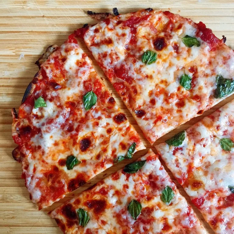 Homemade tortilla pizza topped with melted cheese, pepperoni, and herbs on a wooden cutting board