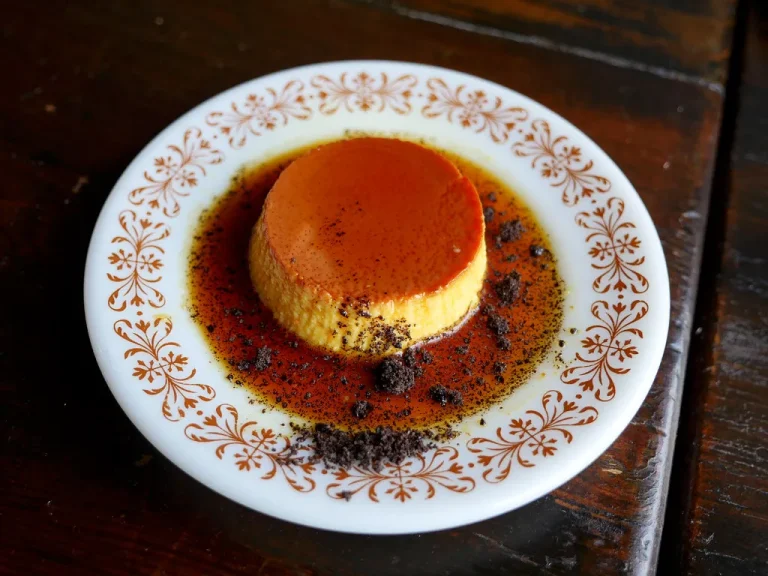 Classic Cuban flan de leche with golden caramel sauce on a white plate, garnished with mint leaves.