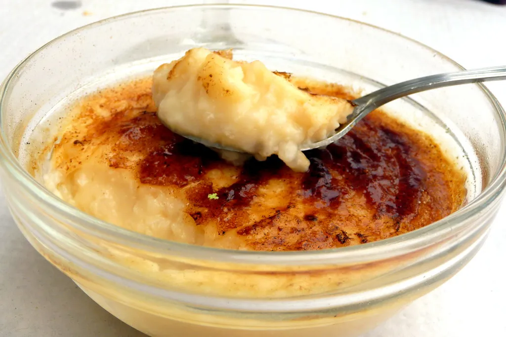 Creamy Cuban arroz con leche served in a white bowl, topped with ground cinnamon and a cinnamon stick.