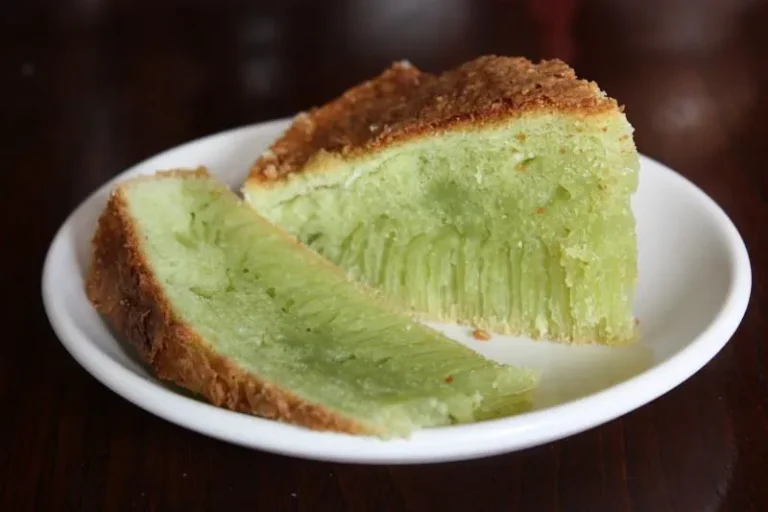 Traditional Vietnamese Bánh Bò cake sliced to reveal its green honeycomb texture, served on a wooden plate with grated coconut on the side.