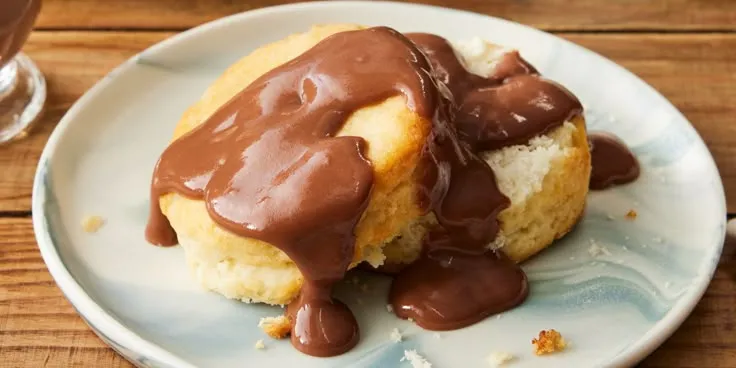 Southern-style biscuits topped with warm, rich chocolate gravy served on a white plate with a fork, perfect for breakfast or brunch.