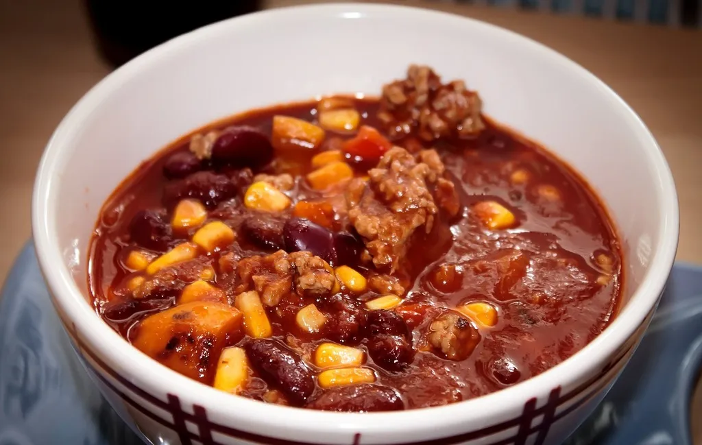 Hearty chili con carne with ground beef, kidney beans, and red chili peppers, garnished with sour cream and fresh cilantro in a rustic bowl.