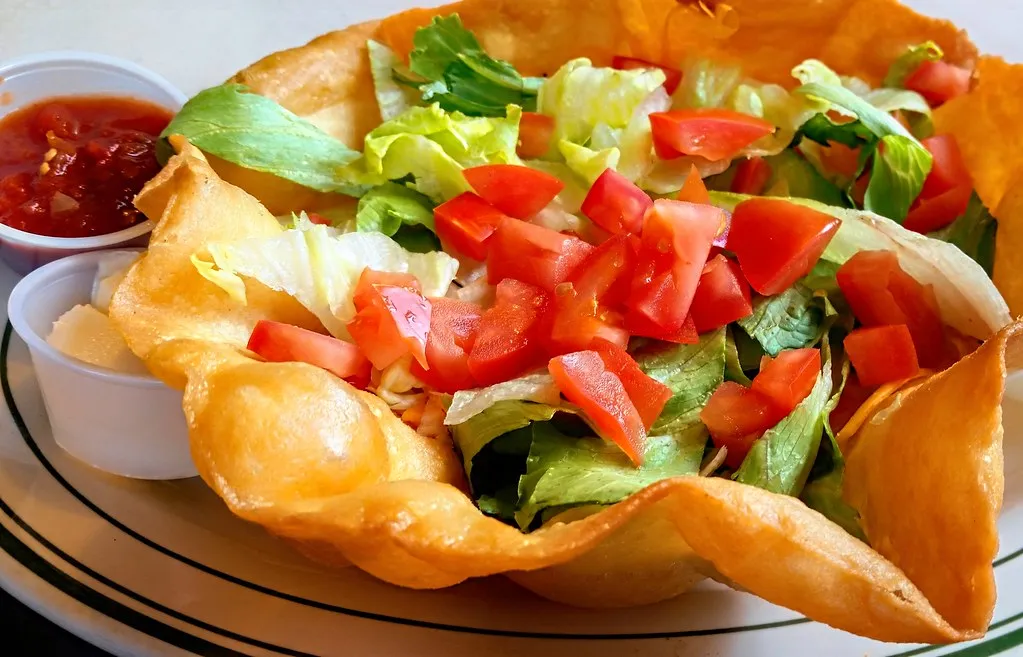 Classic taco salad in a bowl with seasoned ground beef, lettuce, cherry tomatoes, shredded cheese, sour cream, and crushed tortilla chips.