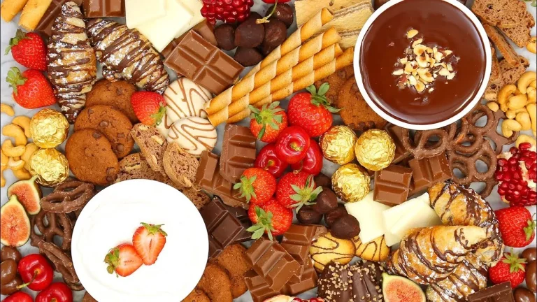 A beautifully styled dessert board featuring an assortment of chocolates, fresh fruits, cookies, and sweet dips on a rustic wooden platter