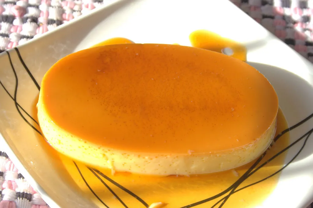 Classic Cuban flan de leche with golden caramel sauce on a white plate, garnished with mint leaves.