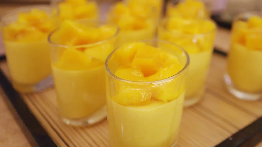 Creamy mango mousse cups topped with fresh mint leaves, served in clear dessert glasses on a tropical-themed dessert table.