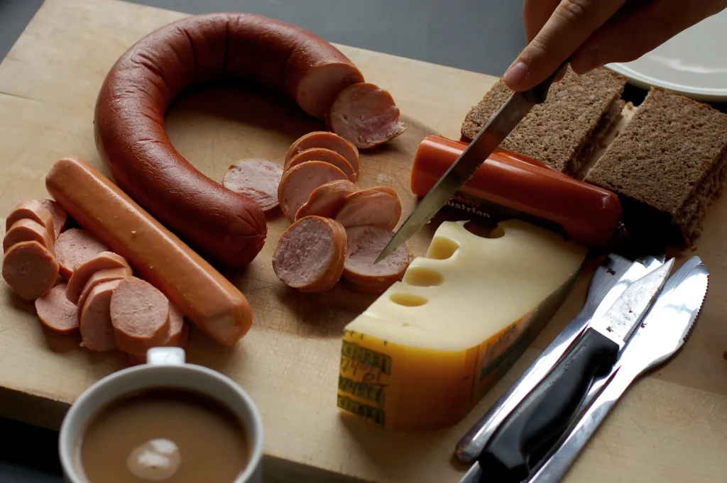 Juicy homemade cheese sausages stacked on a wooden cutting board with melted cheese oozing out