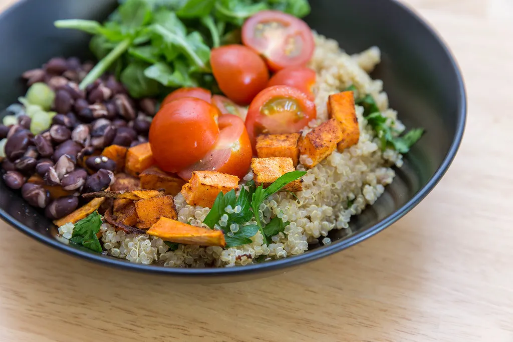 A colorful and balanced dinner plate featuring roasted sweet potatoes, quinoa, leafy greens, and grilled salmon on a white dish.