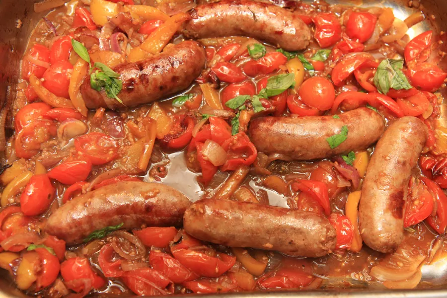 Skillet filled with hot Italian sausage slices, red and green bell peppers, and caramelized onions