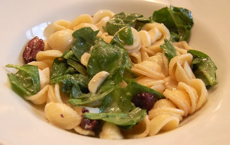 Fresh spinach pasta salad with cherry tomatoes, red onion, and feta in a white serving bowl, dressed with olive oil and herbs.