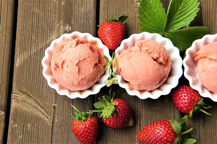 Homemade strawberries and cream ice cream in a bowl topped with fresh strawberry slices and a sprig of mint