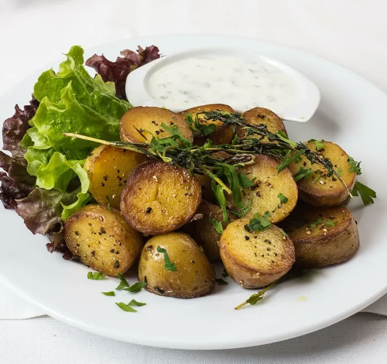Golden baked baby potatoes with crispy skins, seasoned with garlic, herbs, and olive oil, served in a white baking dish.