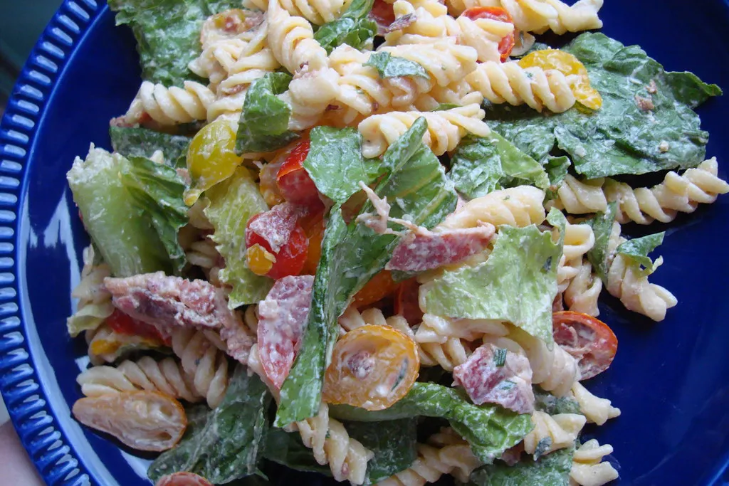Overhead view of a colorful BLT salad in a large white bowl, featuring crispy bacon, lettuce, cherry tomatoes, and creamy dressing