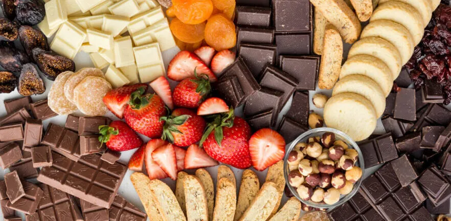 A beautifully arranged dessert board with chocolate truffles, fresh strawberries, kiwi slices, cookies, and caramel dip on a wooden platter