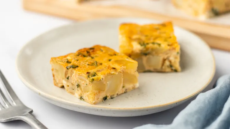 “A golden, fluffy slice of homemade Starbucks potato chive bake served on a white plate with fresh chives and melted cheese on top