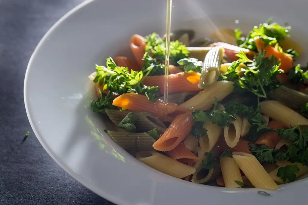 Healthy spinach pasta salad served in a white bowl, featuring fresh baby spinach, whole wheat pasta, and Mediterranean vegetables.