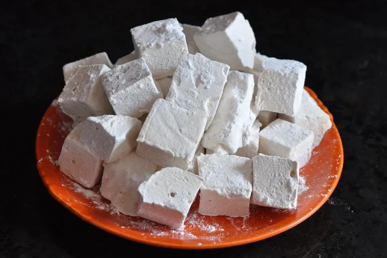 Soft, fluffy homemade marshmallows cut into cubes and dusted with powdered sugar on a white plate