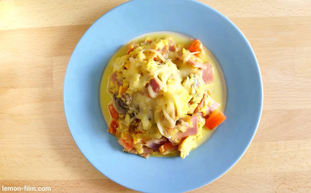 Close-up of a cheesy breakfast skillet with melted cheddar, eggs, crispy bacon, and fresh herbs in a cast iron pan.
