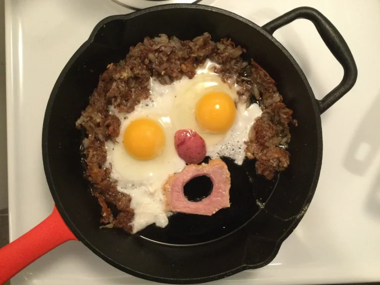 Hearty classic bacon and egg skillet with crispy potatoes, melted cheddar cheese, and fresh chives served in a cast iron pan.
