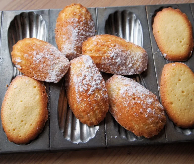 Fluffy French madeleines with golden shells, dusted with powdered sugar and served with tea