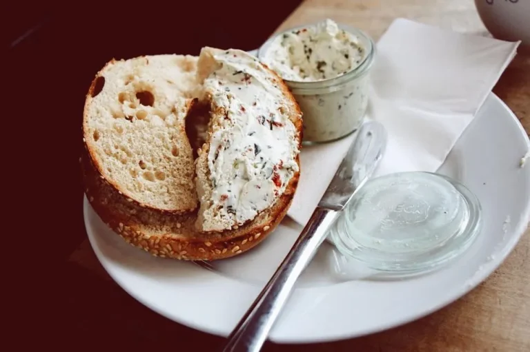 Homemade cream cheese spread on a toasted bagel with fresh herbs and a side of lemon and milk
