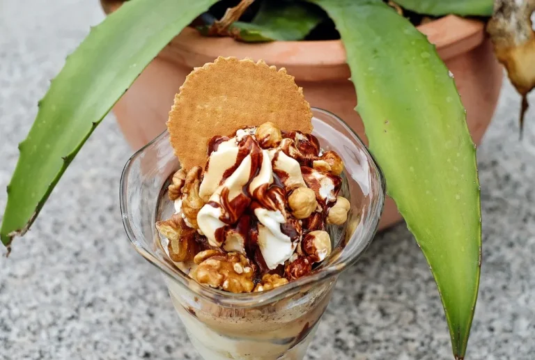 Delicious ice cream sundae with vanilla scoops, hot fudge, whipped cream, nuts, and a cherry served in a glass bowl
