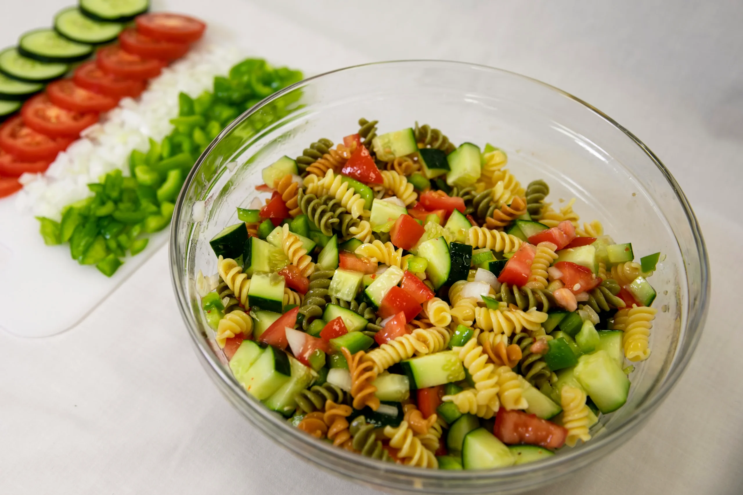Vibrant pasta salad with rotini pasta, cherry tomatoes, cucumbers, black olives, shredded mozzarella, and Italian vinaigrette