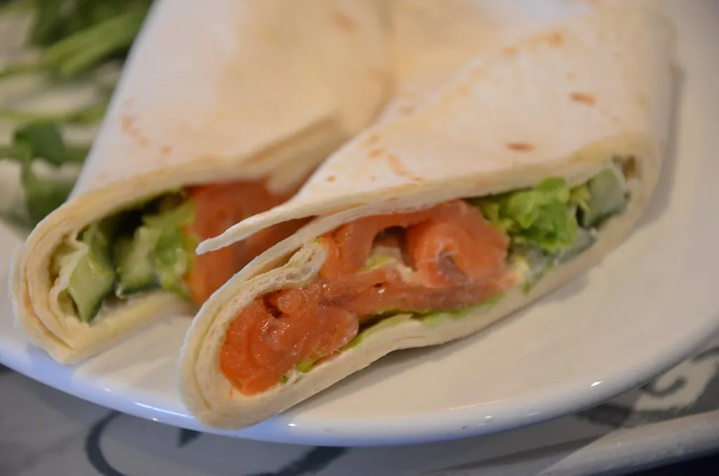 Whole wheat wrap filled with scrambled eggs, smoked salmon, baby spinach, and cream cheese, sliced in half.