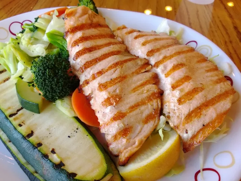Steamed mixed vegetables in a white bowl with fresh herbs and lemon wedges