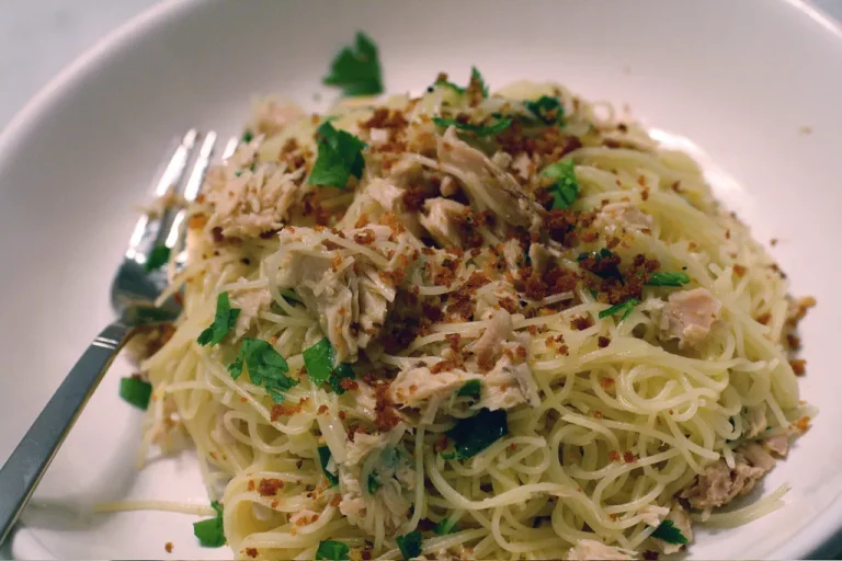 Quick tuna pasta served in a white bowl, topped with parsley, lemon zest, and grated Parmesan, on a rustic wooden table