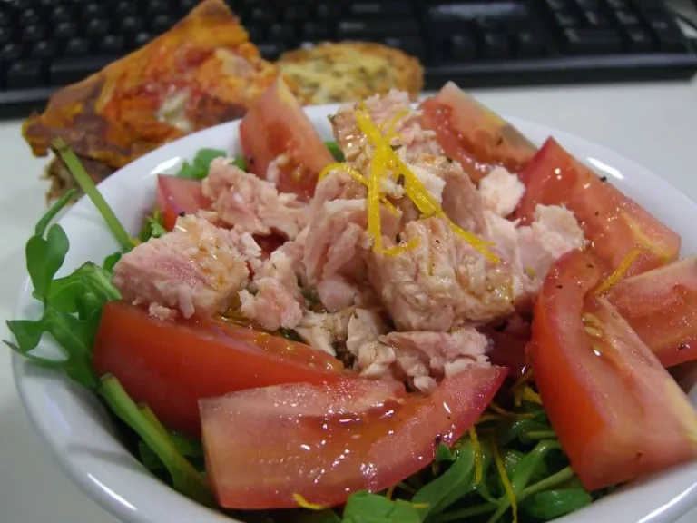 Colorful Mediterranean tuna salad with chickpeas, cherry tomatoes, cucumbers, Kalamata olives, and feta cheese in a white bowl, garnished with lemon wedges and fresh parsley.