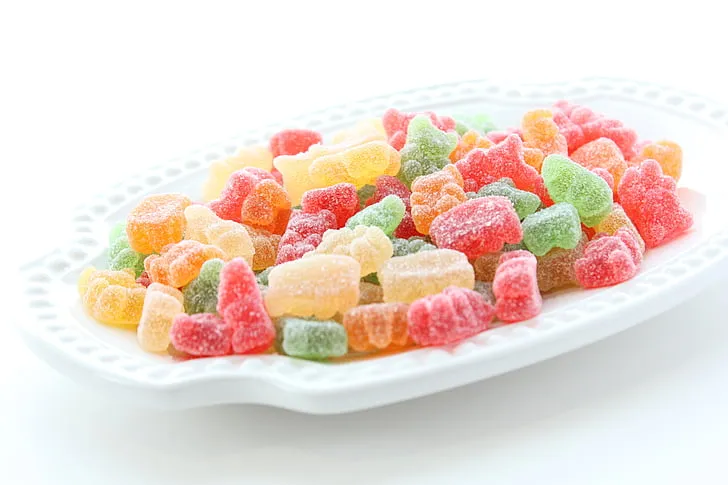 Colorful tropical gummy candies shaped like mango, pineapple, and passion fruit on a white plate