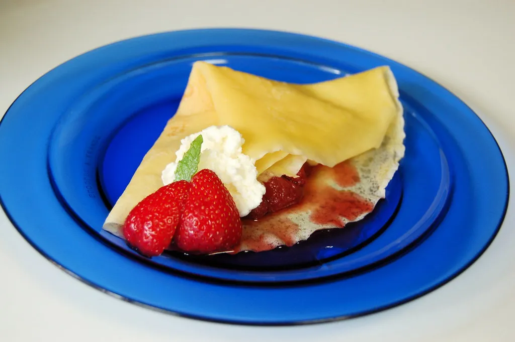 Fresh homemade strawberry crepes topped with whipped cream and powdered sugar