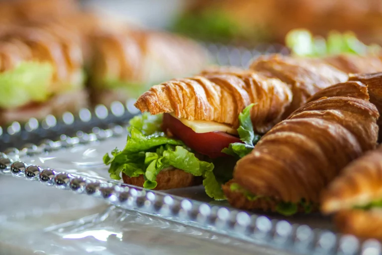 Freshly baked crescent roll breakfast sandwiches with eggs, cheese, and ham on a wooden board