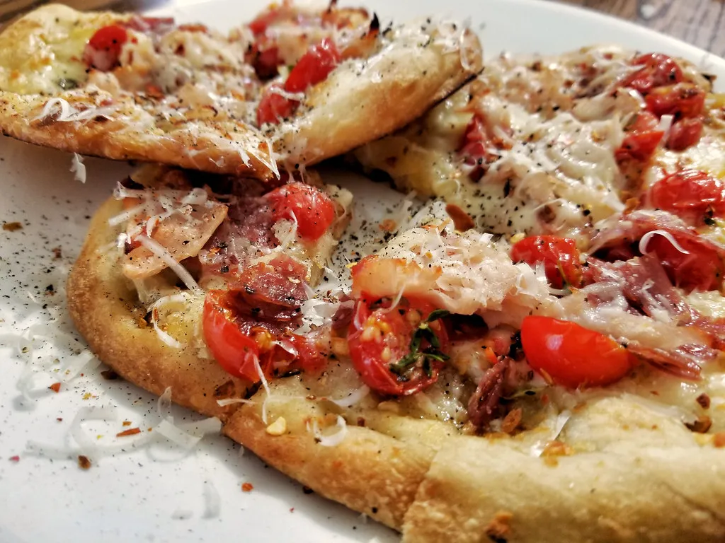 Homemade naan pizza with melted mozzarella, fresh basil, and colorful vegetable toppings on a wooden cutting board