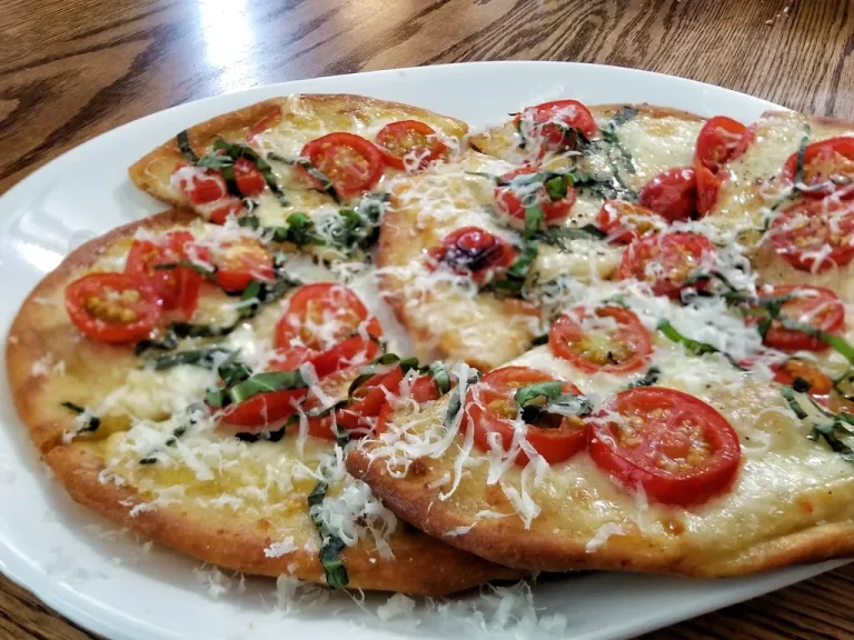 Homemade naan pizza with melted mozzarella, fresh basil, and colorful vegetable toppings on a wooden cutting board